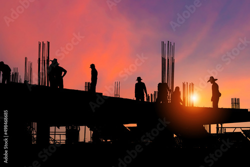 Silhouette of Foreman worker team at construction site with blurred sunset sky background