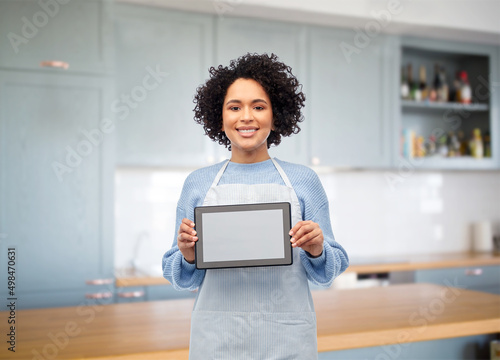 cooking, culinary and people concept - happy smiling woman in apron showing tablet pc computer over home kitchen background