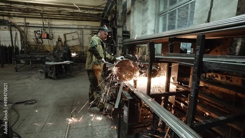 Heavy Industry Engineering Factory Interior with Industrial Worker Using Angle Grinder and Cutting a Metal Tube. Contractor in Safety Uniform and Hard Hat Manufacturing Metal Structures. a worker with