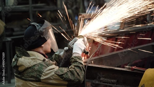 Heavy Industry Engineering Factory Interior with Industrial Worker Using Angle Grinder and Cutting a Metal Tube. Contractor in Safety Uniform and Hard Hat Manufacturing Metal Structures. a worker with