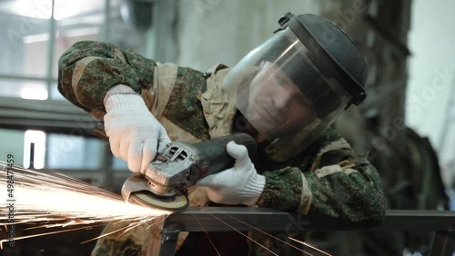 Heavy Industry Engineering Factory Interior with Industrial Worker Using Angle Grinder and Cutting a Metal Tube. Contractor in Safety Uniform and Hard Hat Manufacturing Metal Structures. a worker with
