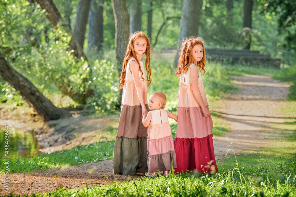 Three red-haired sisters in long linen dresses blow bubbles in the park on sunny summer day. Three red-haired sisters in long linen dresses blow bubbles in the park on sunny summer day.