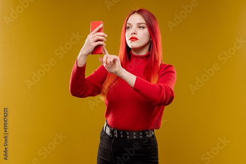 Glamour woman with red hair using smartphone on yellow background