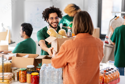 charity, donation and volunteering concept - happy smiling male volunteer giving box of food to woman at distribution center at distribution or refugee assistance center