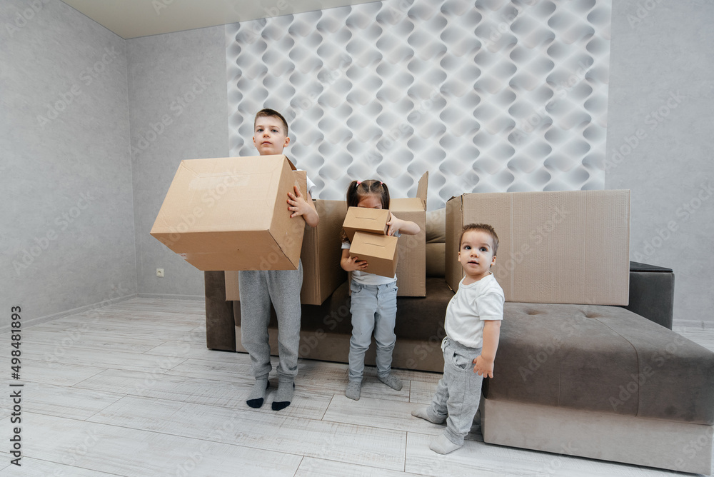 Brothers and sister are playing and enjoying moving to a new apartment against the background of cardboard boxes and a sofa. Purchase of real estate. Housewarming, delivery. Brothers and sister are playing and enjoying moving to a new apartment against the background of cardboard boxes and a sofa. Purchase of real estate. Housewarming, delivery.