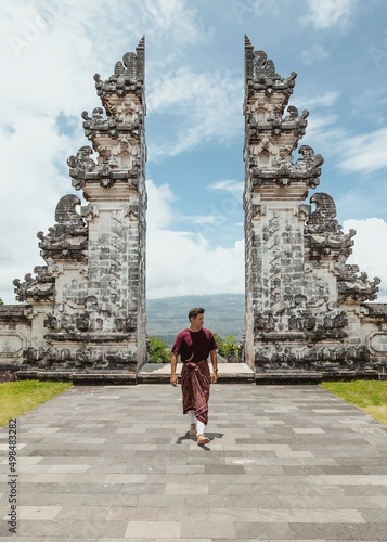 young male tourist wearing a traditional balinese sarong walking in front of gates of heaven temple in north bali indonesia