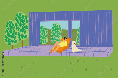 Woman enjoys the nature while sits on sunbed on wooden terrace near the modern house with panoramic windows near pine forest whith big white dog. Concept of solitude and recreation on nature