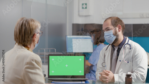 Senior woman and medic looking at greenscreen on laptop, during covid 19 pandemic. Elder patient and physician using blank chromakey template with isolated mockup background and copyspace.