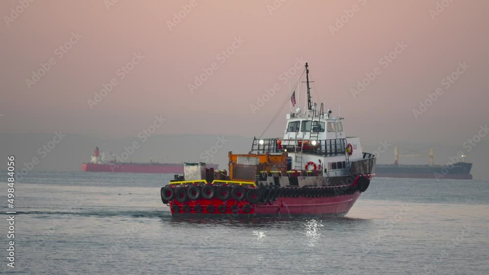 A tugboat turns out to sea with container ships in the background during a colorful sunrise A tugboat turns out to sea with container ships in the background during a colorful sunrise