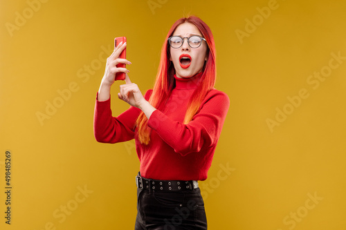 Glamour woman wearing glasses using smartphone on yellow background
