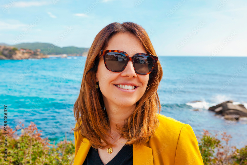 Face shot portrait of cheerful young brunette woman on the beach wears yellow suit and sunglasses. Happy smiling businesswoman looking away. Copy space. Face shot portrait of cheerful young brunette woman on the beach wears yellow suit and sunglasses. Happy smiling businesswoman looking away. Copy space.