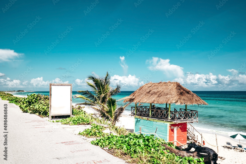tropical landscape of a hut on a white sand beach in cozumel mexico with turquoise blue ocean and a beach umbrella with chairs setup on a sunny day