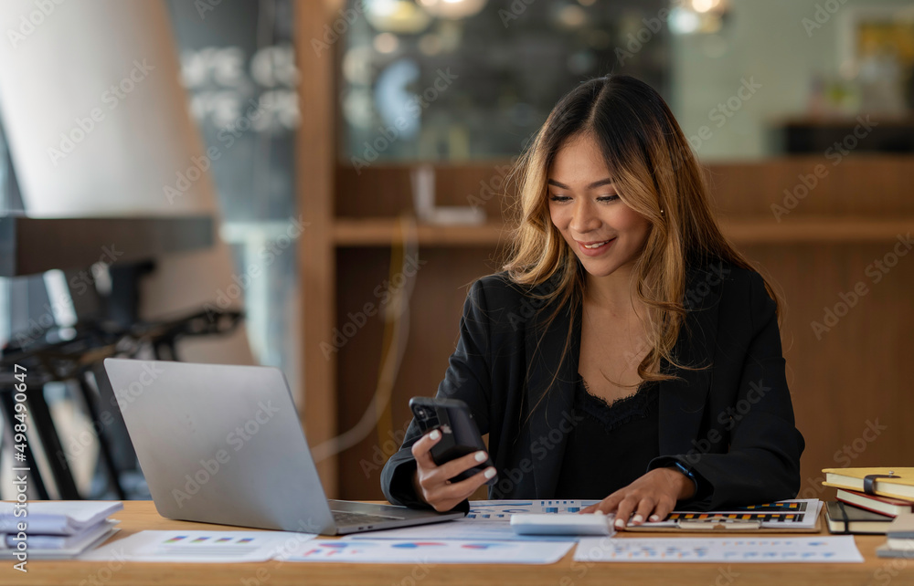 Portrait of young asian woman sitting at her desk with laptop and adhesive notes using mobile phone. Asian businesswoman working in modern office. Portrait of young asian woman sitting at her desk with laptop and adhesive notes using mobile phone. Asian businesswoman working in modern office.