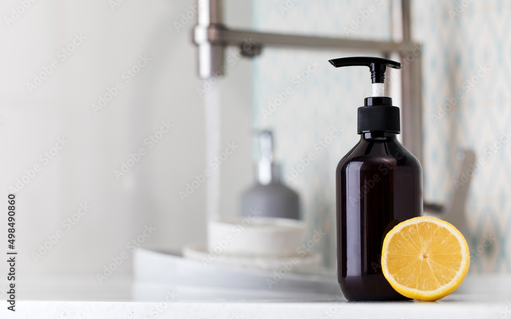 Bottle with eco friendly dishwashing detergent with lemon on the background of a sink with dirty dishes.