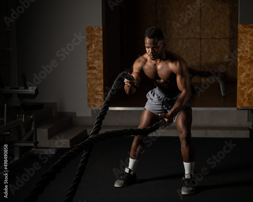 Attractive african american man with naked torso doing endurance exercises with trope. 