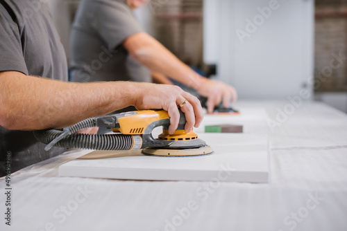 An employee of a furniture factory sands a wooden surface with a sander photo