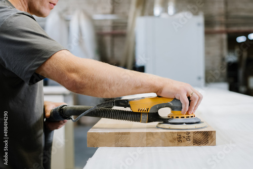 An employee of a furniture factory sands a wooden surface with a sander photo