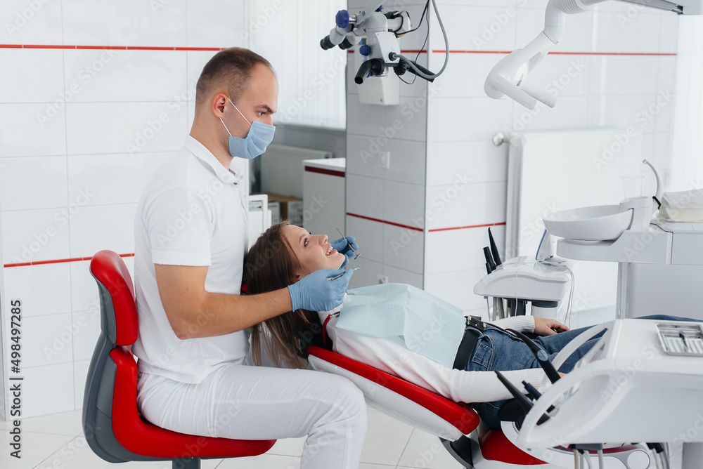 Fototapeta premium A young dentist specialist examines and treats the teeth of a beautiful woman in modern white dentistry. Dental prosthetics, treatment and teeth whitening. Modern dentistry.