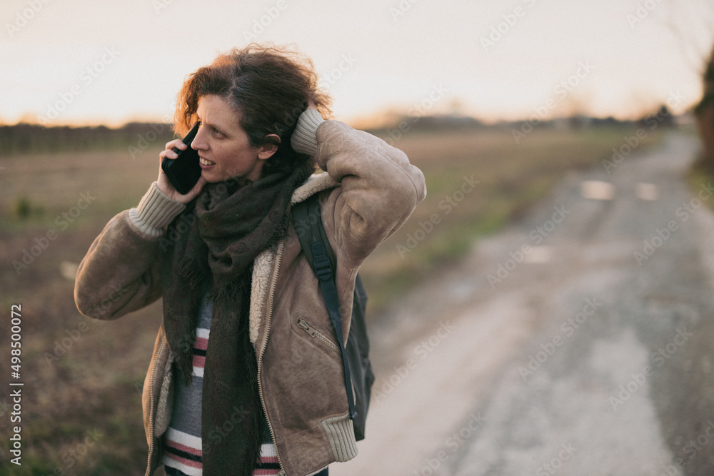 Winter walk of Curly hair woman with a phone trough countryside at sunset copy space