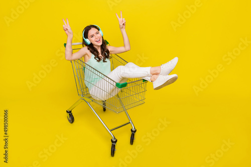 Full body portrait of crazy lady sit trolley show v-sign enjoy wireless stereo song isolated on yellow color background