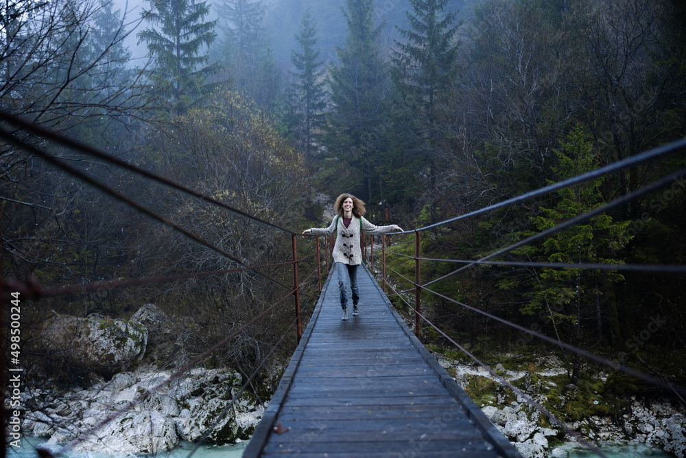 Happy Woman Hiker crossing a Hanging bridge in winter wilderness Slovenia