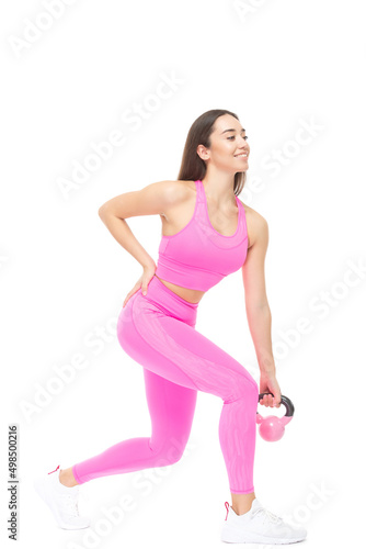 A beautiful, athletic, slim, smiling and cheerful woman in a pink tracksuit performs exercises with a pink kettlebell. Lifestyle concept with sports and gym. Isolated on white background.