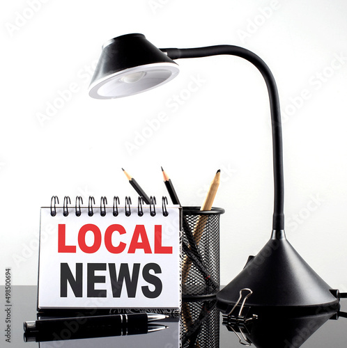 LOCAL NEWS text on notebook with pen and table lamp on the black background photo