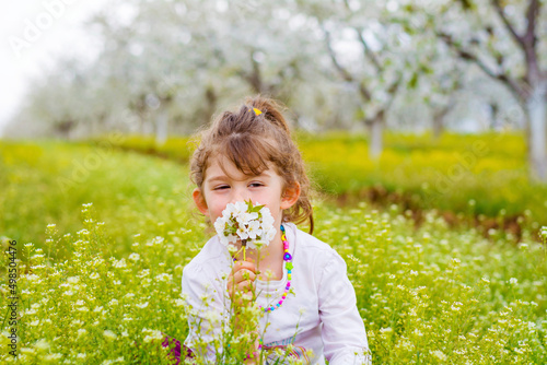 Happy toddler girl sitting on a meadow with blooming cherry trees .Spring time 