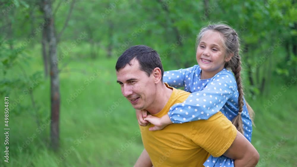 Piggyback family in park. Happy family at picnic in park. Father day in summer on green grass. Picnic in forest park. Daughter play with her father in a forest park. Happy child play on the grass Piggyback family in park. Happy family at picnic in park. Father day in summer on green grass. Picnic in forest park. Daughter play with her father in a forest park. Happy child play on the grass