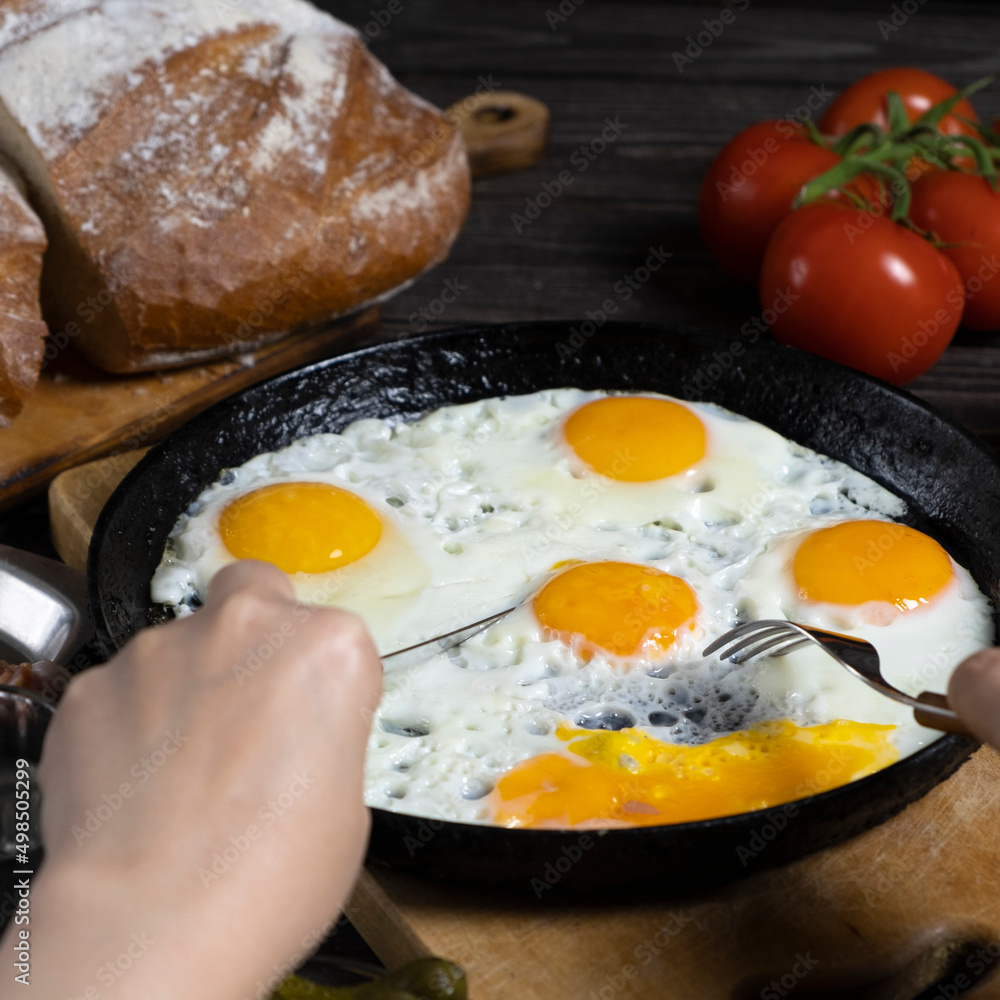Cooked breakfast - scrambled eggs in pan, tomatoes, bread kitchen table. Female hands with knife and fork Cooked breakfast - scrambled eggs in pan, tomatoes, bread kitchen table. Female hands with knife and fork