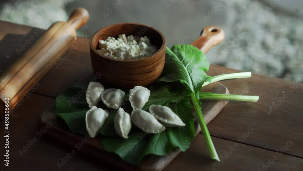 Traditional Russian fresh handmade dumplings lying on a wooden table on a cutting board with cottage cheese in a wooden plate and spinach Traditional Russian fresh handmade dumplings lying on a wooden table on a cutting board with cottage cheese in a wooden plate and spinach