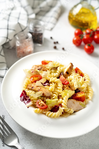 Pasta salad with grilled chicken, tomatoes and olive oil in a plate on a light culinary background. Traditional Italian dish girandole or fusilli fried poultry fillet and vegetables closeup	