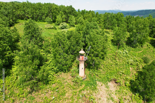 An old lighthouse on a mountain covered with forest on a summer day. Aerial view.