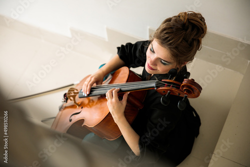 female cellist sits on stairs and plays cello with fingers, pizzicato technique, enjoys performing music, top view, suitable for poster or poster