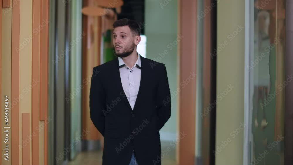 Young handsome serious man walking along corridor in office and thinking. Portrait of Caucasian businessman strolling at workplace. Confident successful male CEO looking around Young handsome serious man walking along corridor in office and thinking. Portrait of Caucasian businessman strolling at workplace. Confident successful male CEO looking around