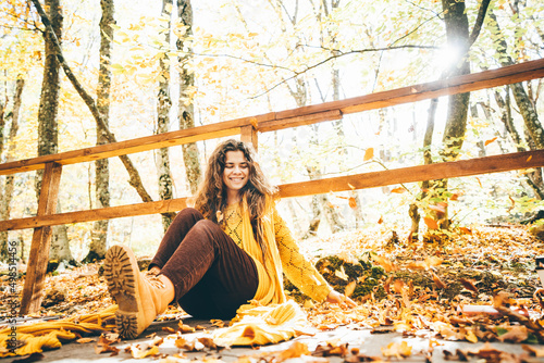  Brunette woman in yellow sweater sitting on a fallen autumn leaves in a park. © Mariia Korneeva