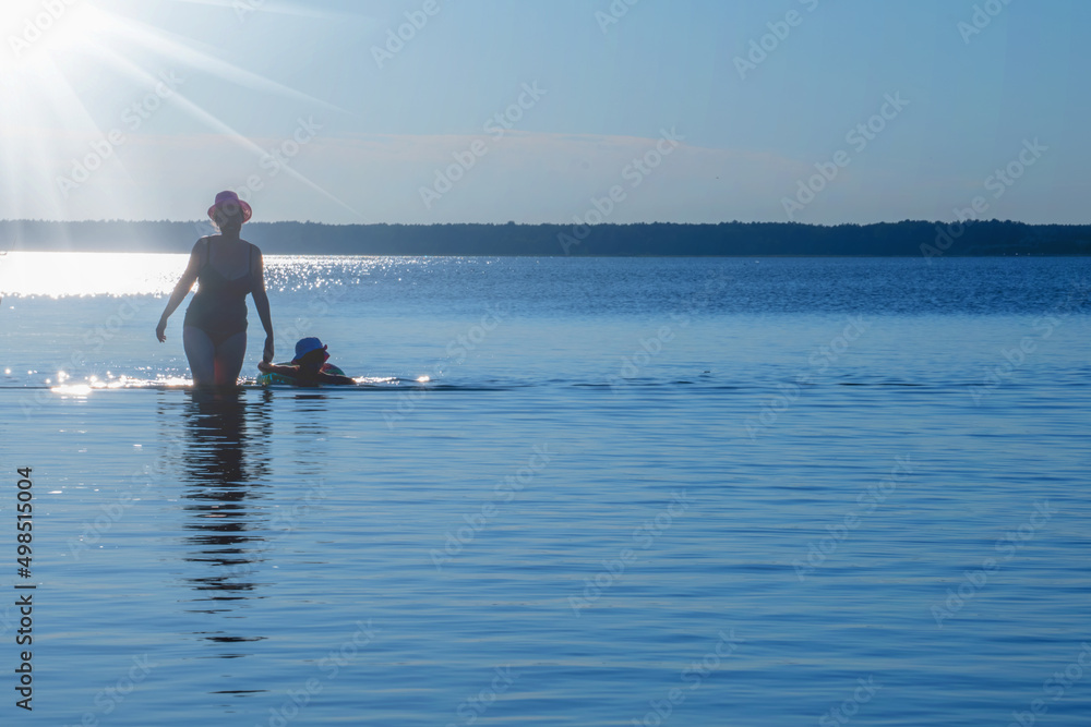 Silhouette of a woman and child in the water. Landscape of beautiful tranquil sea. Summer holiday, rest and travel concept. Horizontal image. Copy space.