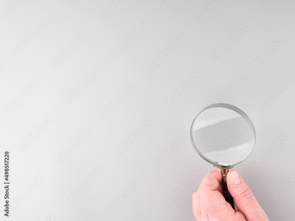 Magnifying glass in a hand on a gray background. Space for text Magnifying glass in a hand on a gray background. Space for text