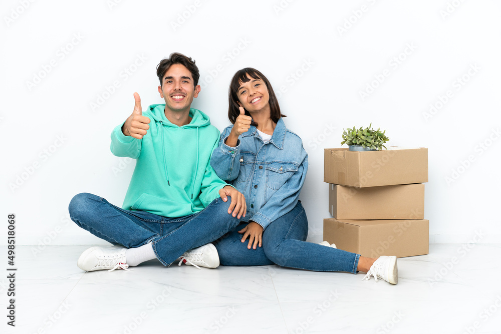 Young couple making a move while picking up a box full of things sitting on the floor isolated on white background giving a thumbs up gesture because something good has happened