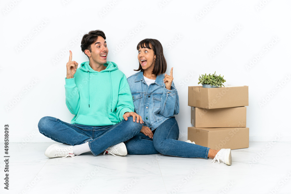 Young couple making a move while picking up a box full of things sitting on the floor isolated on white background intending to realizes the solution while lifting a finger up Young couple making a move while picking up a box full of things sitting on the floor isolated on white background intending to realizes the solution while lifting a finger up