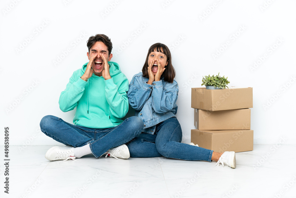 Young couple making a move while picking up a box full of things sitting on the floor isolated on white background shouting and announcing something