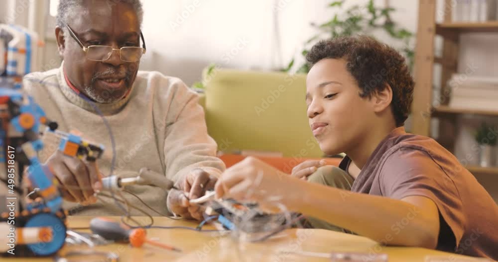 A granddad and his grandchild building a robot at home. A granddad and his grandchild building a robot at home.