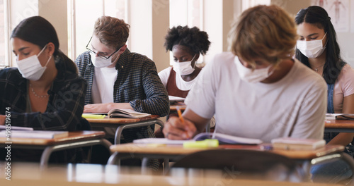 Nothing gets in their way of getting that grade. Shot of masked teenagers writing an exam in a classroom. © Kobus L/peopleimages.com