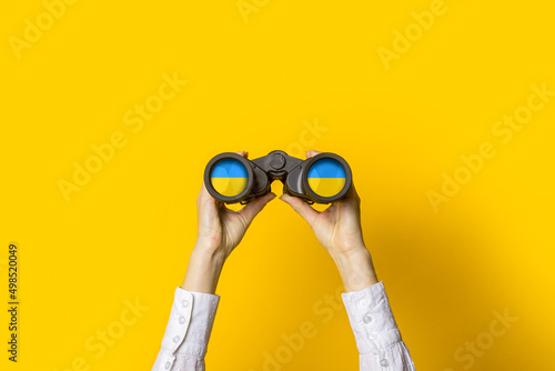 female hands hold black binoculars on a bright yellow background