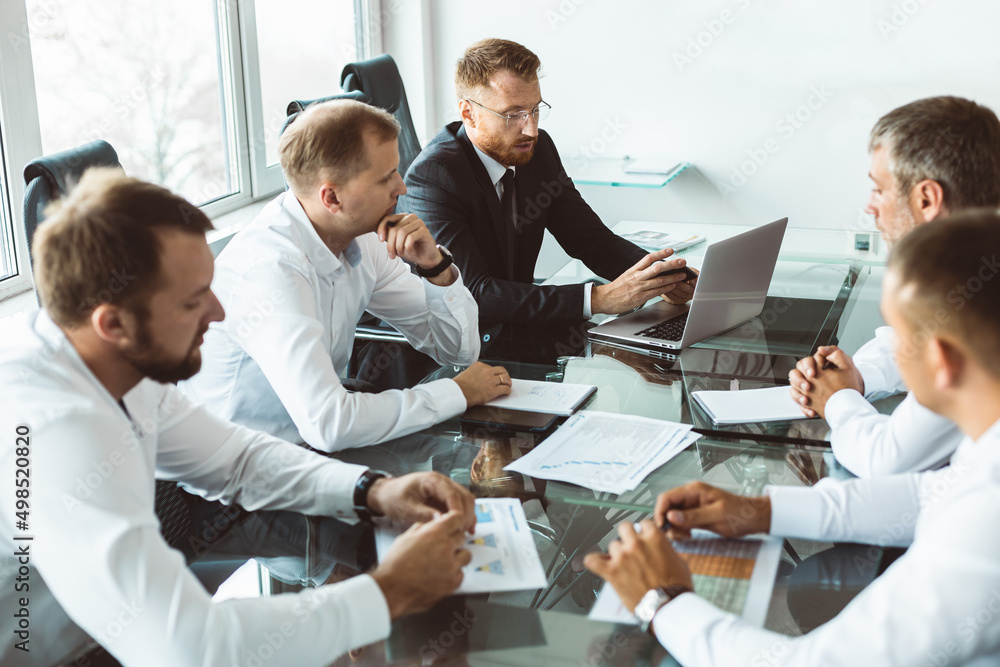 A group of company employees sits at a table in a meeting room. A team of young businessmen working and communicating together in an office. Corporate business team and manager in a meeting