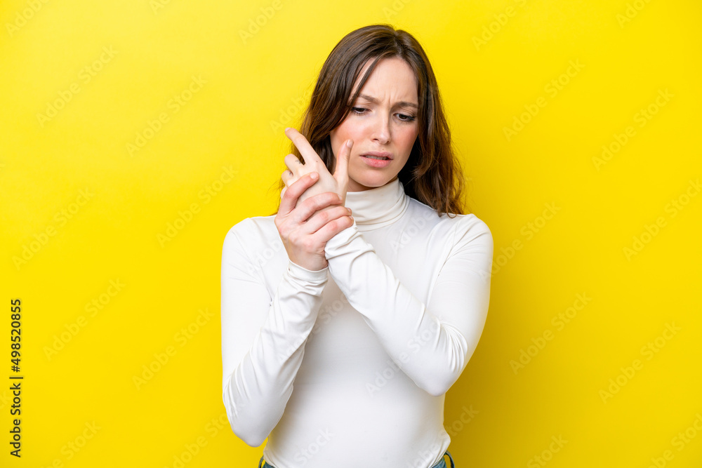 Young caucasian woman isolated on yellow background suffering from pain in hands Young caucasian woman isolated on yellow background suffering from pain in hands