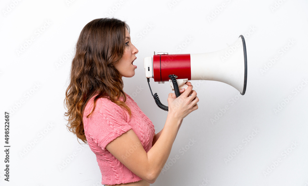 Young caucasian woman isolated on white background shouting through a megaphone to announce something in lateral position