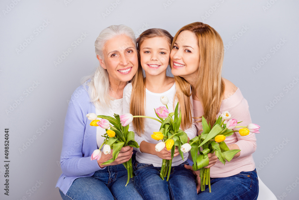 Portrait of three idyllic positive people sitting embrace hold fresh tulips isolated on grey color background Portrait of three idyllic positive people sitting embrace hold fresh tulips isolated on grey color background