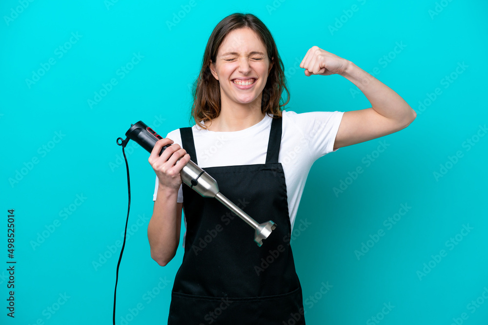 Young caucasian cooker woman using hand blender isolated on blue background doing strong gesture Young caucasian cooker woman using hand blender isolated on blue background doing strong gesture