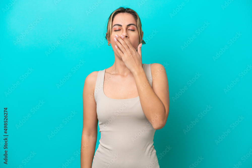 Young caucasian woman isolated on blue background yawning and covering wide open mouth with hand Young caucasian woman isolated on blue background yawning and covering wide open mouth with hand